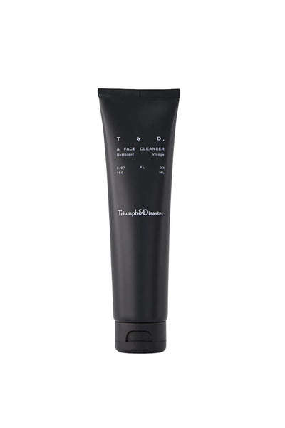 A black tube of Triumph & Disaster Face Cleanser with white text and a flip-top cap stands upright on a plain white background.