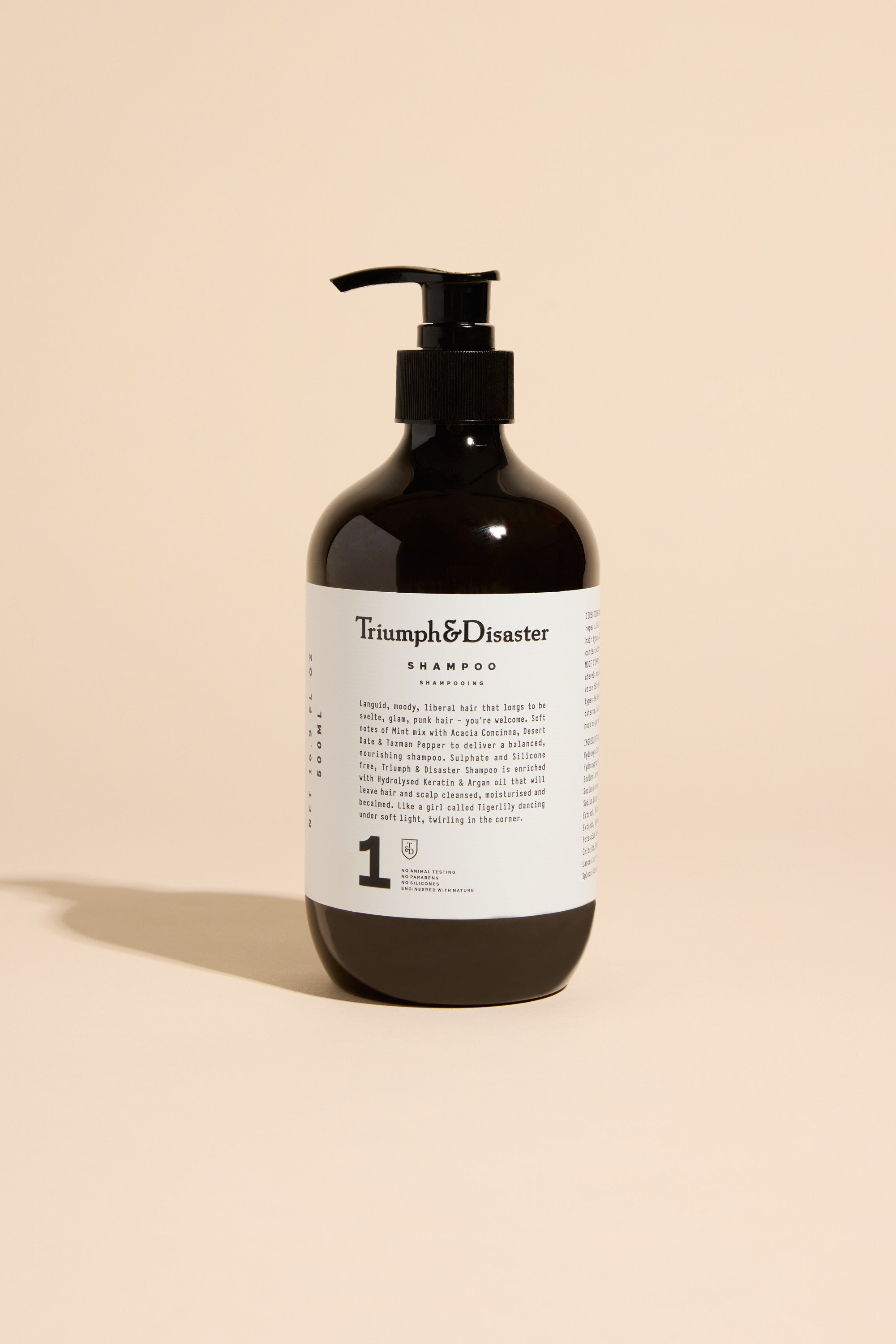 A 500 ml Triumph & Disaster Shampoo bottle with a white label stands upright on a beige background, casting a soft shadow to the left.