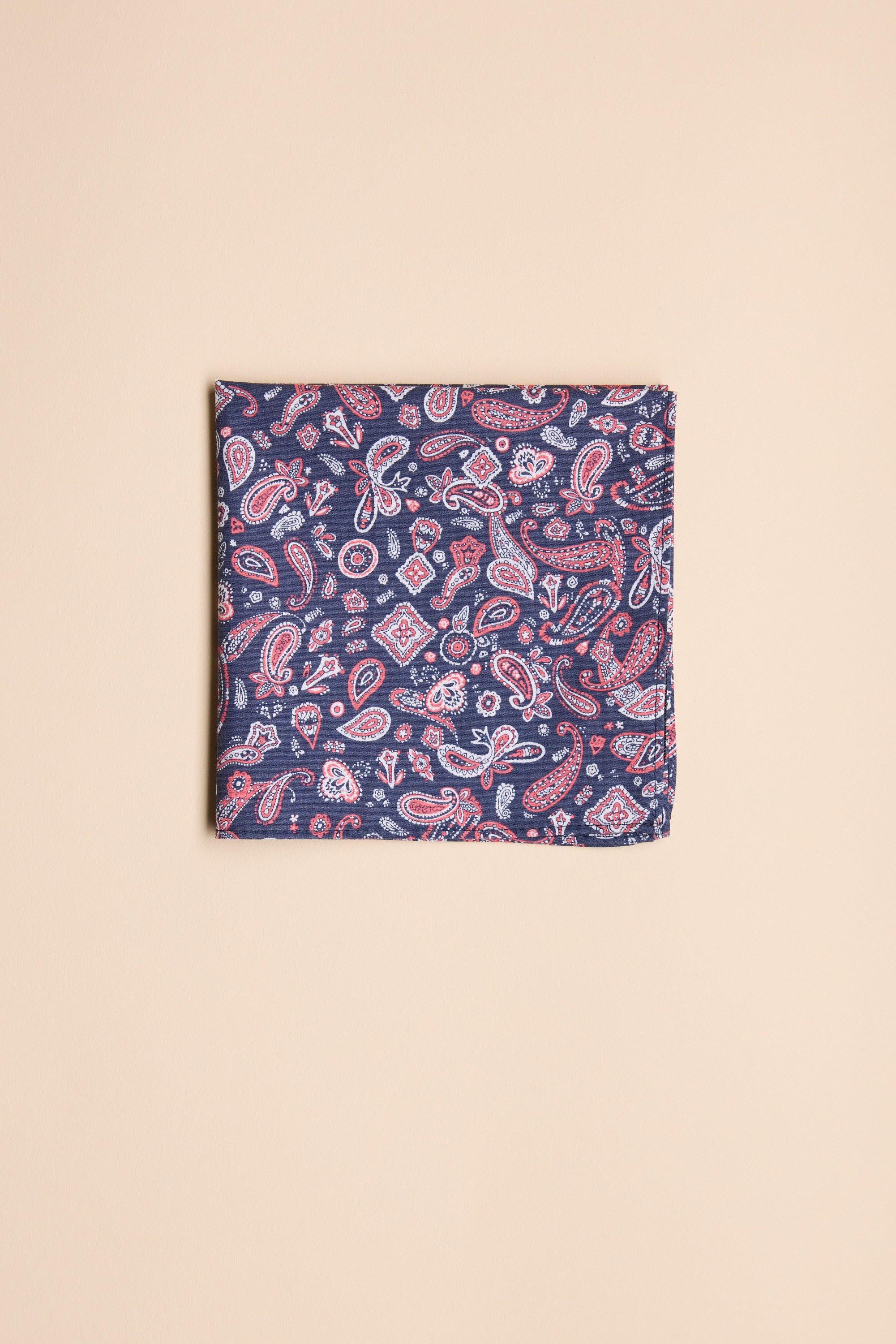 The Barkers Paisley Pocket Square features a blue background with red and white paisley patterns, shown folded on a plain beige surface.
