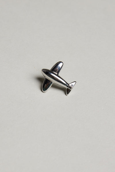 The Barkers Jet Plane Lapel Pin, featuring a polished finish, rests on a plain light gray surface.