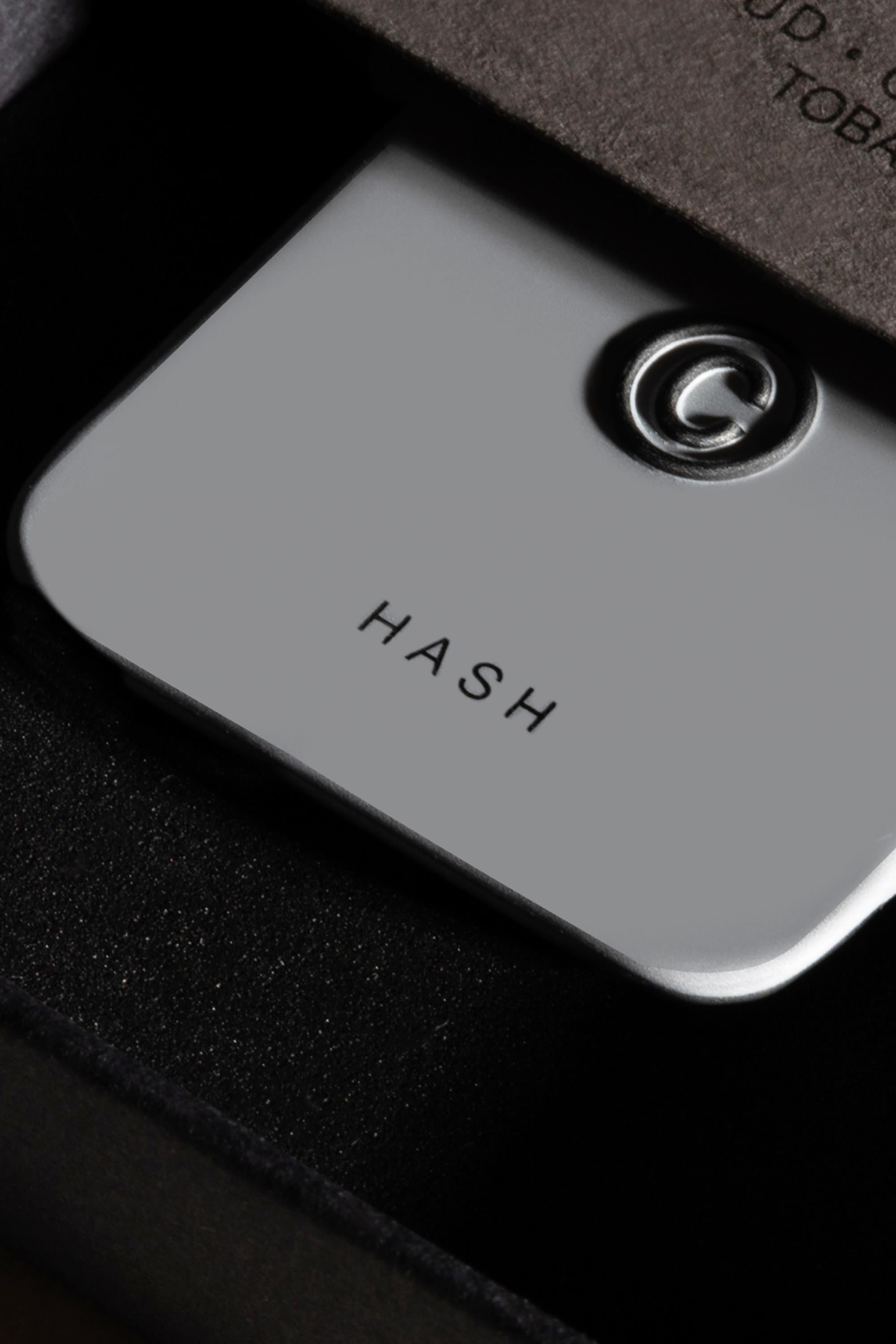 A close-up of Solid State - Hash, a sleek metallic solid state cologne by Solid State with a raised G logo, displayed in a black cushioned box.