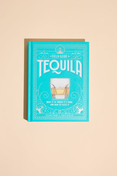 A turquoise book titled "A Field Guide To Tequila" by Other, with a glass of tequila on the cover, is set against a light beige background.