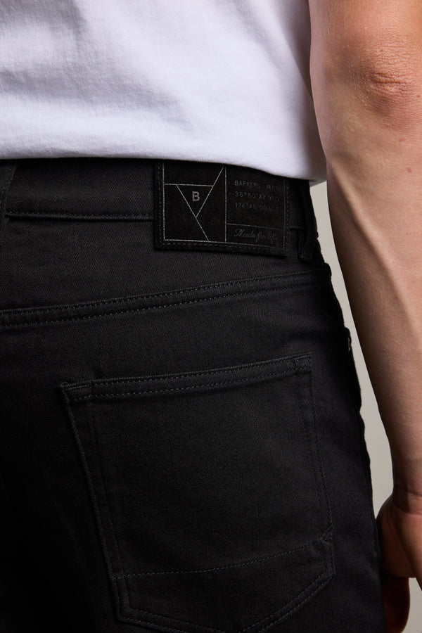 Close-up of a person in Barkers Rambler Denim Slim Jeans and a white shirt, focusing on the back pocket and waistband with a black label—crafted from sustainable denim for style with a conscience.