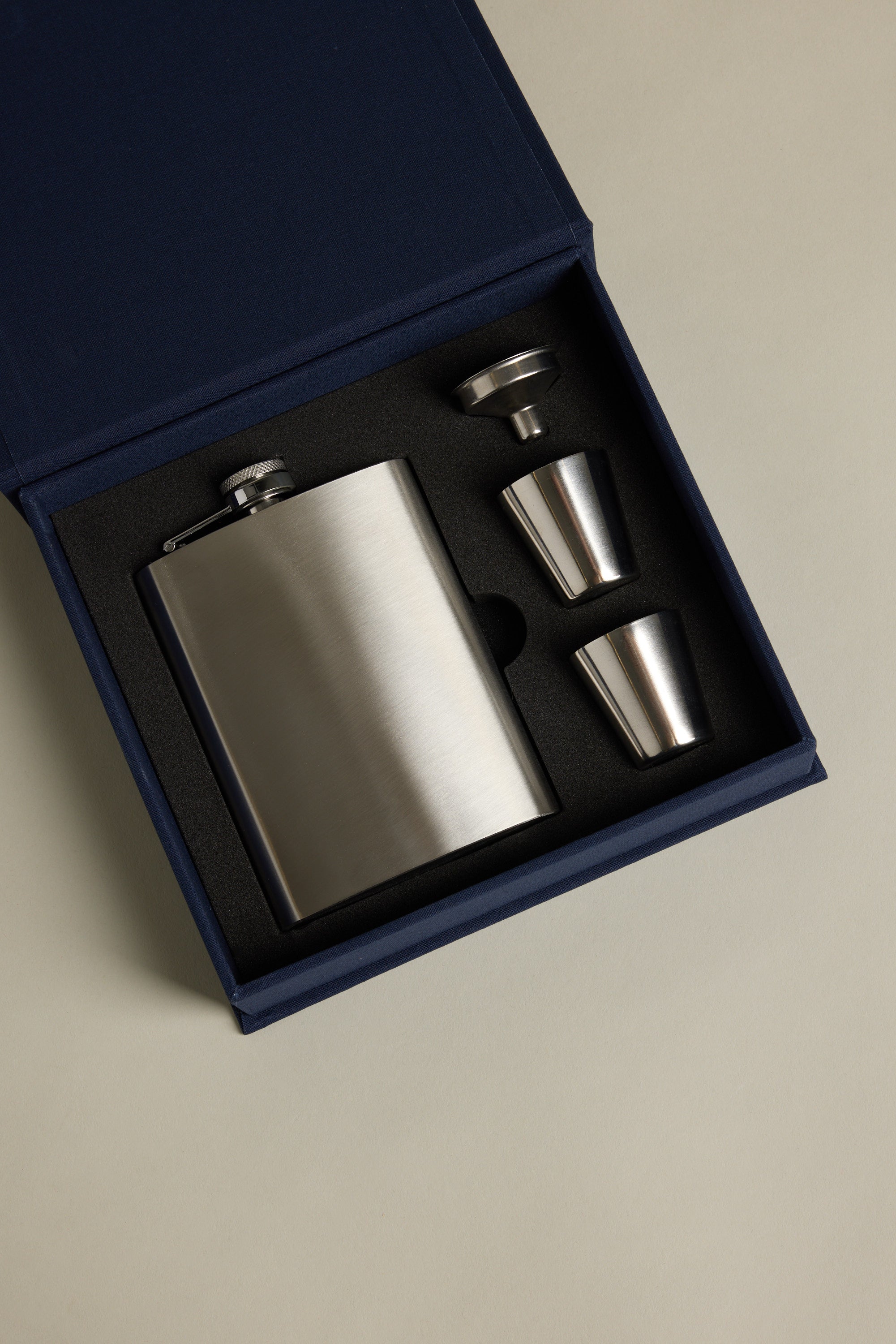 The Barkers "The Essentials Hip Flask" kit comes in a blue gift box with a stainless steel flask, two shot glasses, and a funnel—all securely set in black foam cutouts.