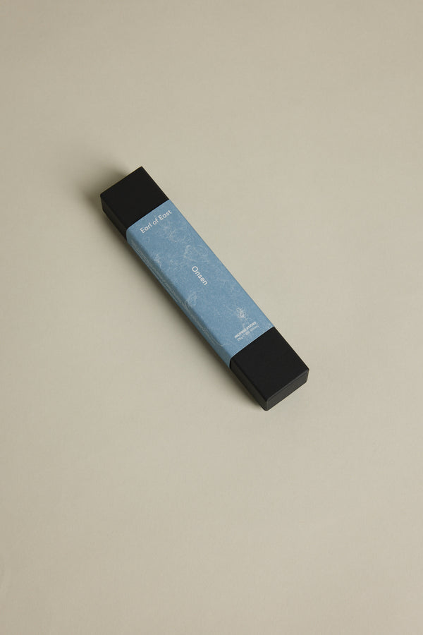 A rectangular box with black ends and a light blue label reading “Earl of East” rests on a beige surface. The label features EoE Onsen Japanese Incense Sticks, evoking the refreshing scent and tranquility of an Onsen bath.
