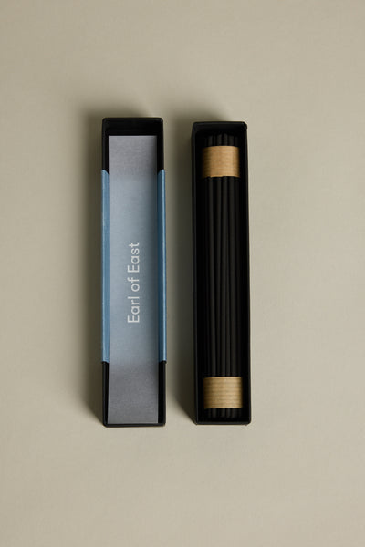 A rectangular black box labeled “Earl of East” holds EoE Onsen Japanese Incense Sticks, each wrapped at the ends with brown paper. The open box and lid rest on a beige surface, inviting a calming Japanese-inspired ritual.