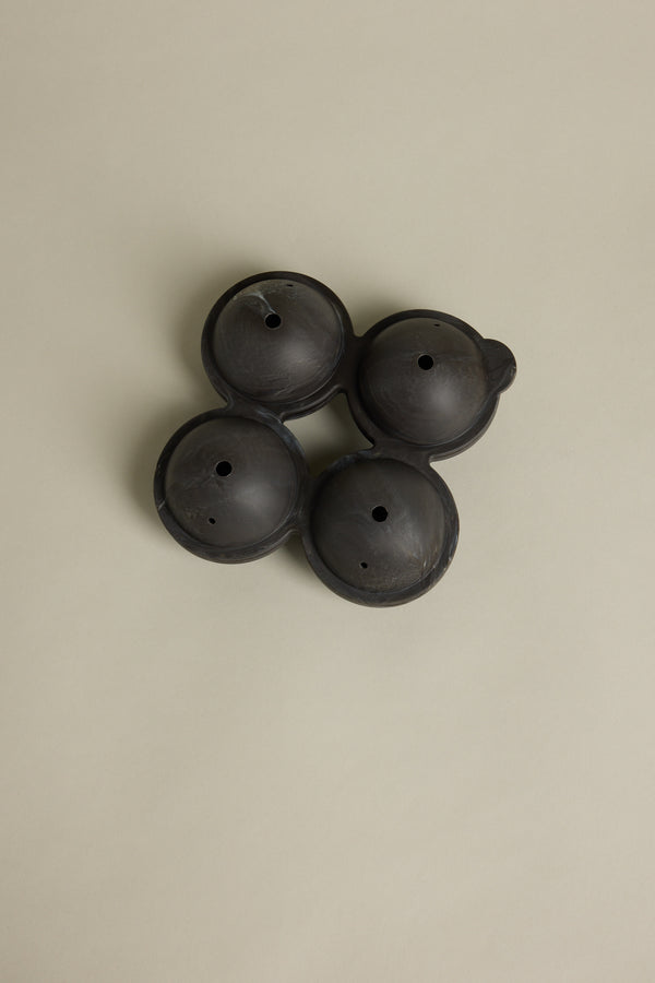 Four Barkers Ice Tray Sphere Marble Black molds, round with small center holes, are interconnected in a square on a beige background—perfect for making large cocktail ice spheres.