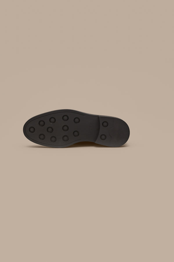 A black rubber sole, featuring circular grips, is displayed against a beige background—an essential detail in quality Portuguese-made men's dress shoes like the Barkers Saville Derby Shoe.