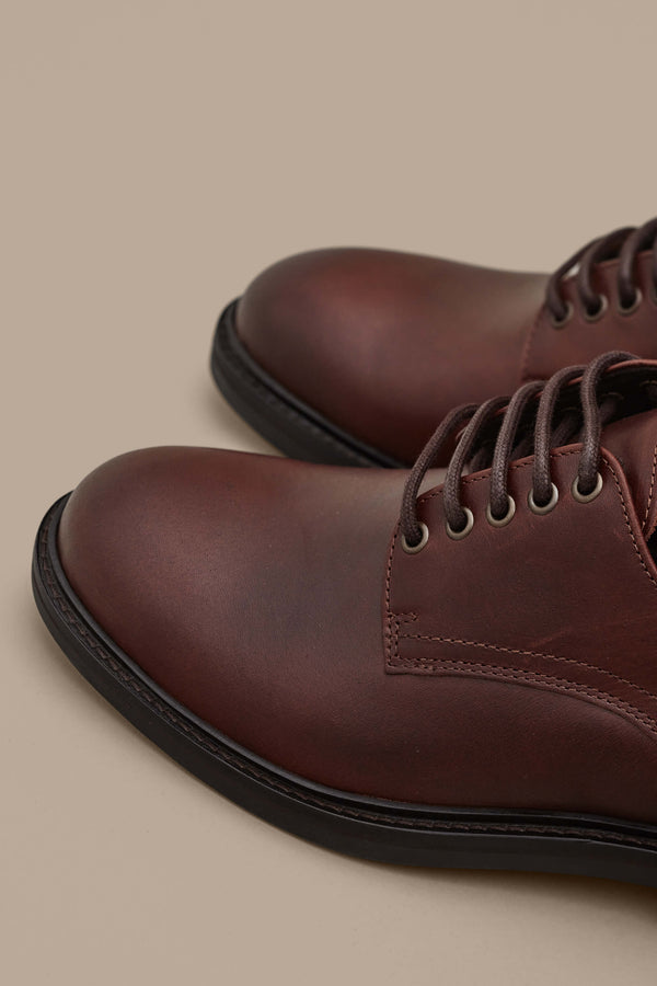 A close-up of the Barkers Saville Derby Shoe—classic brown leather footwear with black soles—spotlights premium Portuguese craftsmanship, set against a neutral beige background.