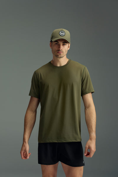 A man faces forward in a WearEver Pulse Tee, an olive green performance t-shirt by WearEver, paired with a matching green cap featuring a circular logo and black shorts, all set against a plain gray background.