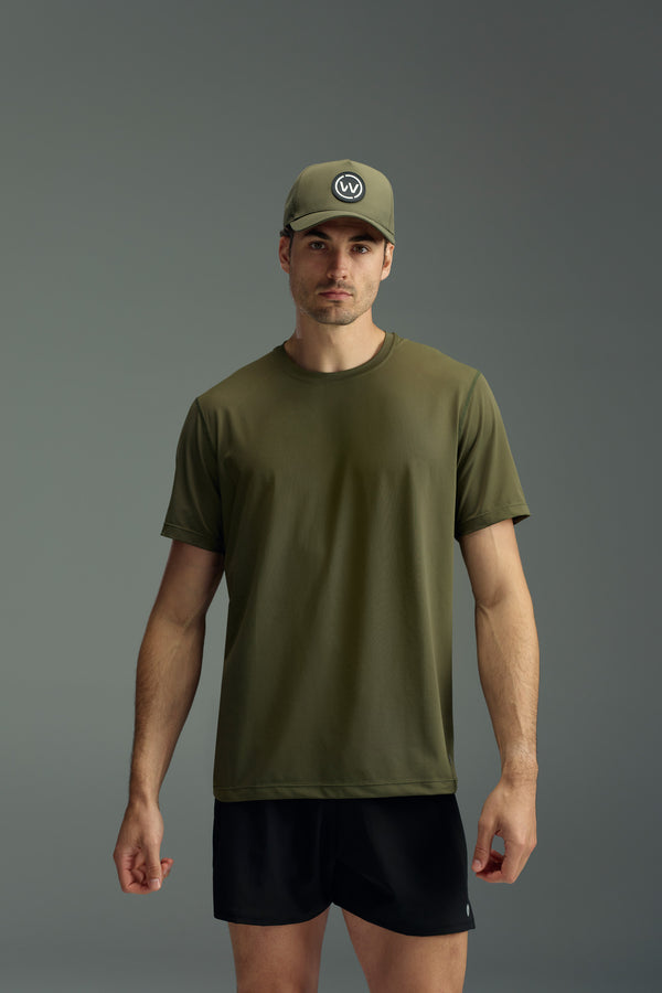 A man faces forward in a WearEver Pulse Tee, an olive green performance t-shirt by WearEver, paired with a matching green cap featuring a circular logo and black shorts, all set against a plain gray background.
