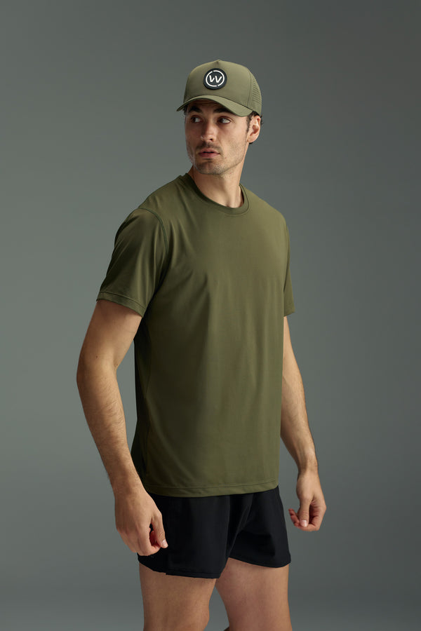 A man wearing a WearEver Pulse Tee in olive green and a matching WearEver logo cap with black shorts stands against a gray background, looking to his left.