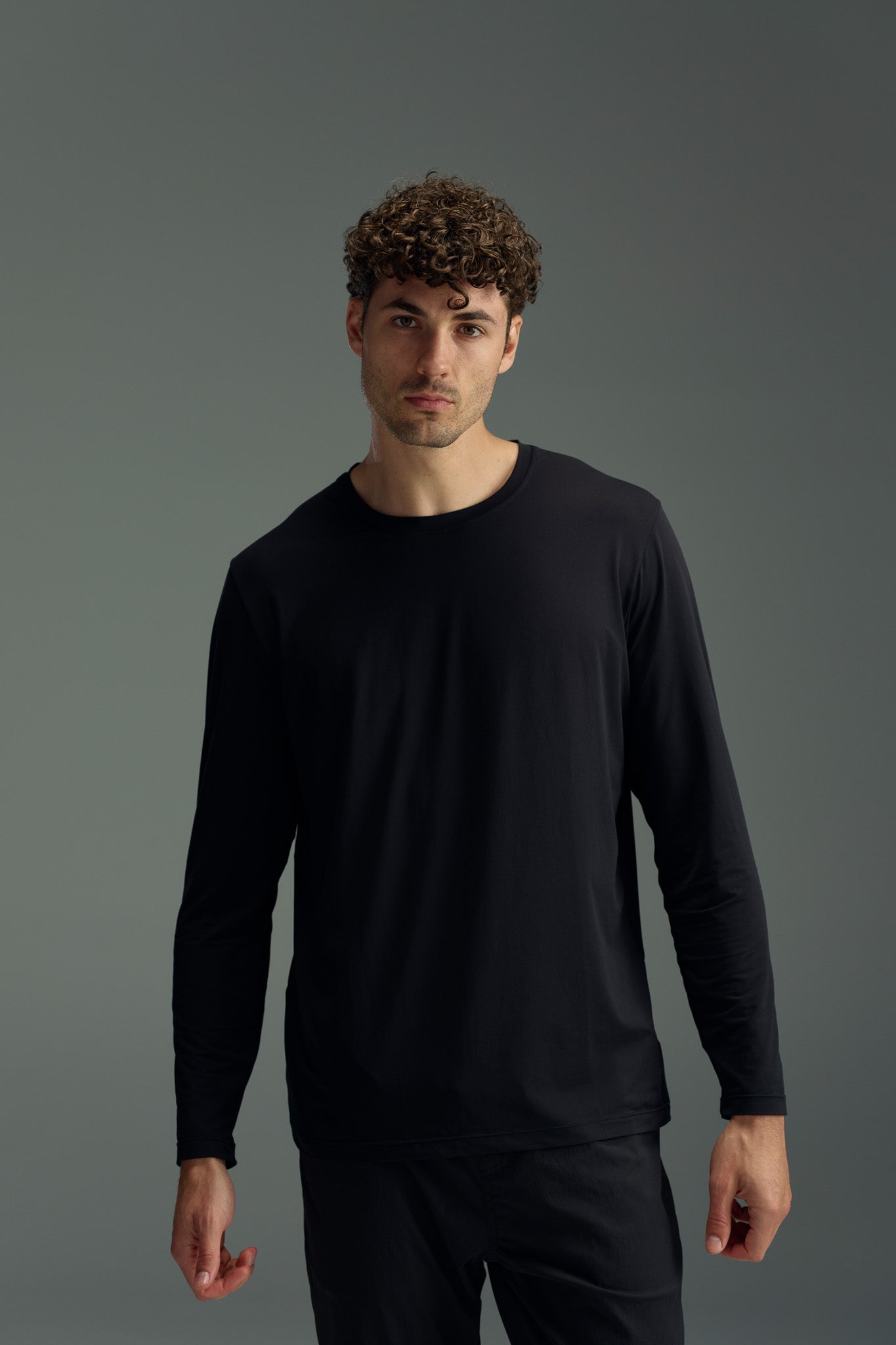 A man with short curly hair wears the WearEver Pulse Long Sleeve Tee by WearEver, standing against a neutral gray background and looking directly at the camera with a neutral expression.