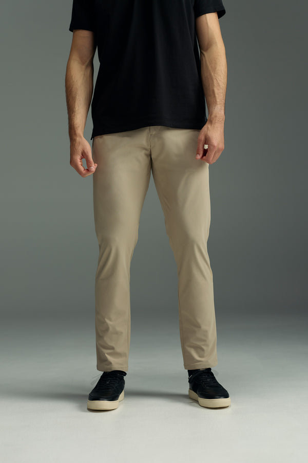 A person stands against a plain background, wearing a black t-shirt, black sneakers, and beige WearEver Long Game Pants by WearEver. The image is cropped at the shoulders, so the person's face is not visible.