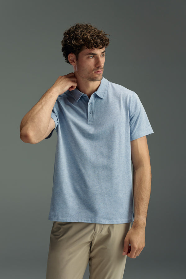 A man with short curly hair wears the WearEver Outbound Polo by WearEver in light blue and beige pants, standing against a plain gray background while touching the back of his neck and looking to the side.