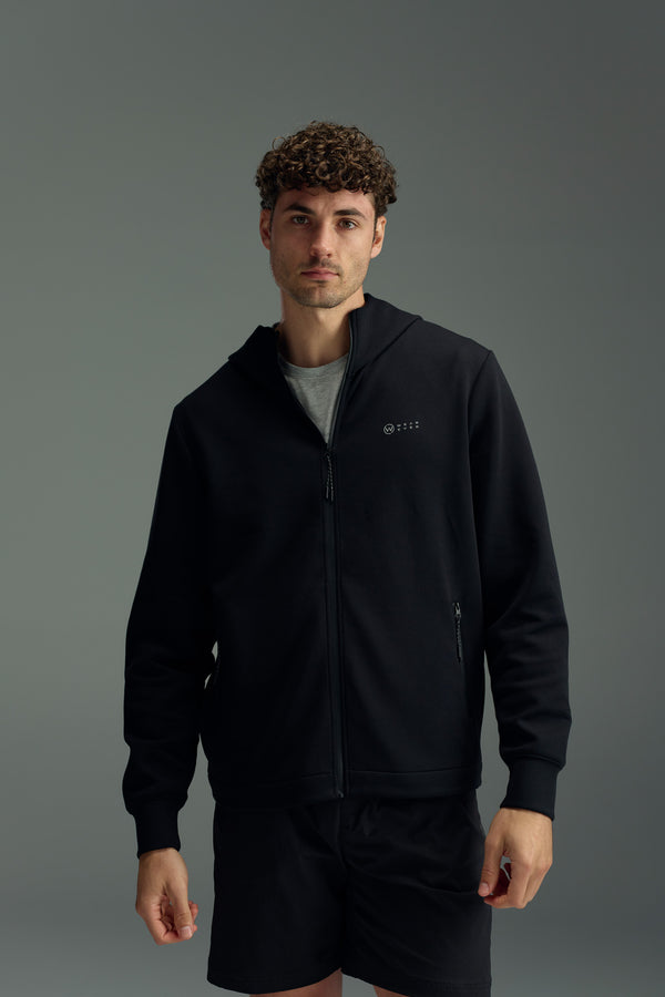 A man with short curly hair wears the WearEver Altitude Hoody by WearEver over a gray shirt and black shorts, standing against a plain gray background and looking directly at the camera with a neutral expression.