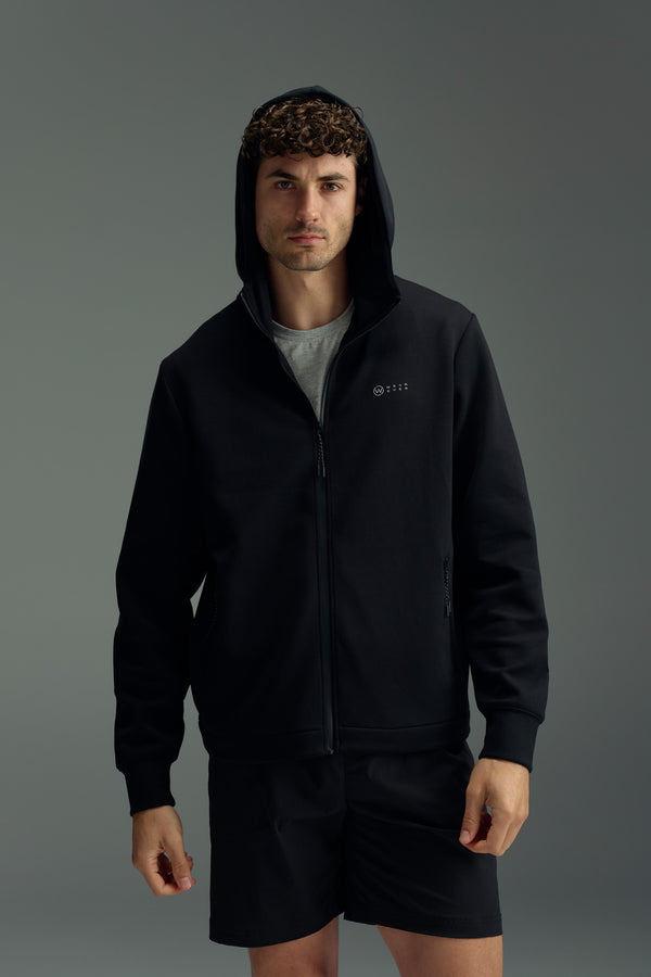 A man faces forward wearing the WearEver Altitude Hoody—black tech fleece zip-up with hood up—over a gray shirt, paired with matching black shorts, all by WearEver, set against a plain gray background.