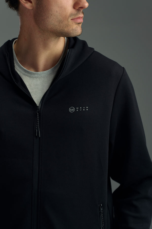 A man wears the WearEver Altitude Hoody, a black tech fleece zip-up with a small WEAREVER logo on the chest, over a light grey t-shirt against a plain grey background.