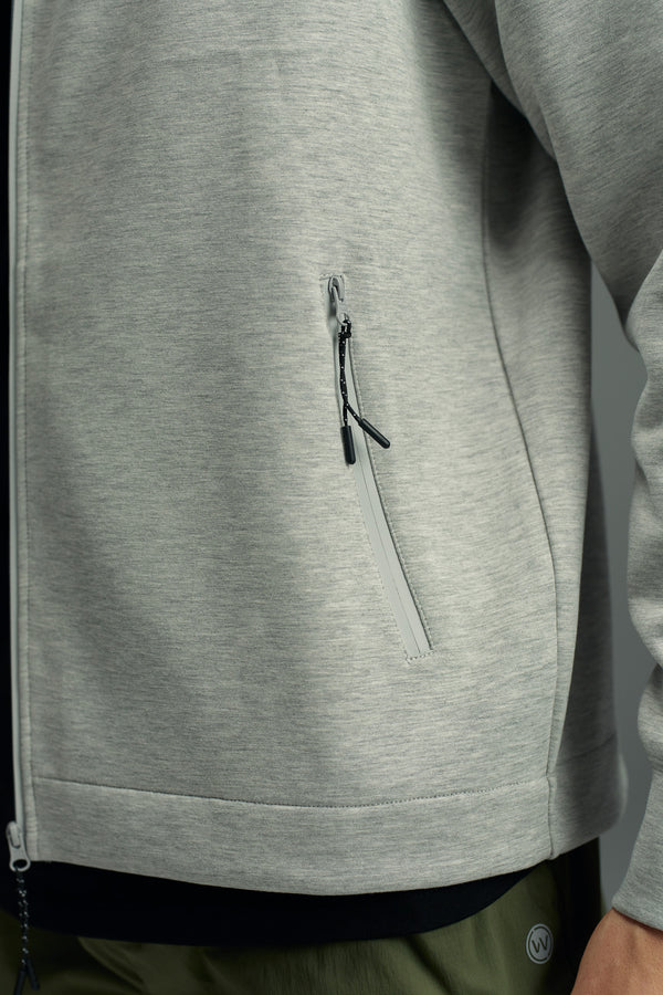 A close-up of a person in the WearEver Altitude Hoody by WearEver, a light gray tech fleece zip-up with a zippered side pocket, showing part of the sleeve and upper section of dark green pants.