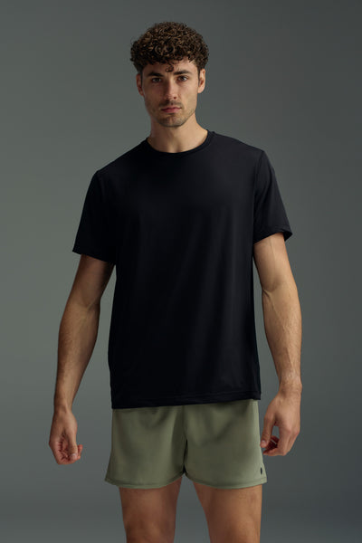 A man with short curly hair wears the WearEver Pulse Tee in black and light olive green athletic shorts, standing against a plain gray background.