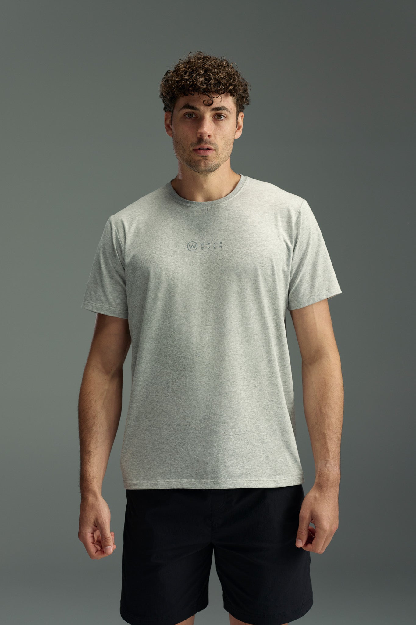A man with short curly hair wears the WearEver Outbound T-Shirt with moisture wicking, paired with black shorts, standing against a plain grey background and facing forward neutrally.