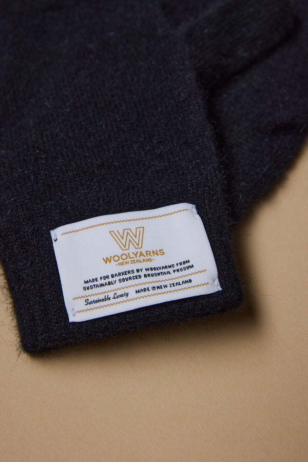 A close-up of NZ Made Perino Gloves by Woolyarns Perino, crafted in New Zealand from a merino, possum, and silk blend. The white label and light brown background highlight the premium, ethically made quality of these gloves.