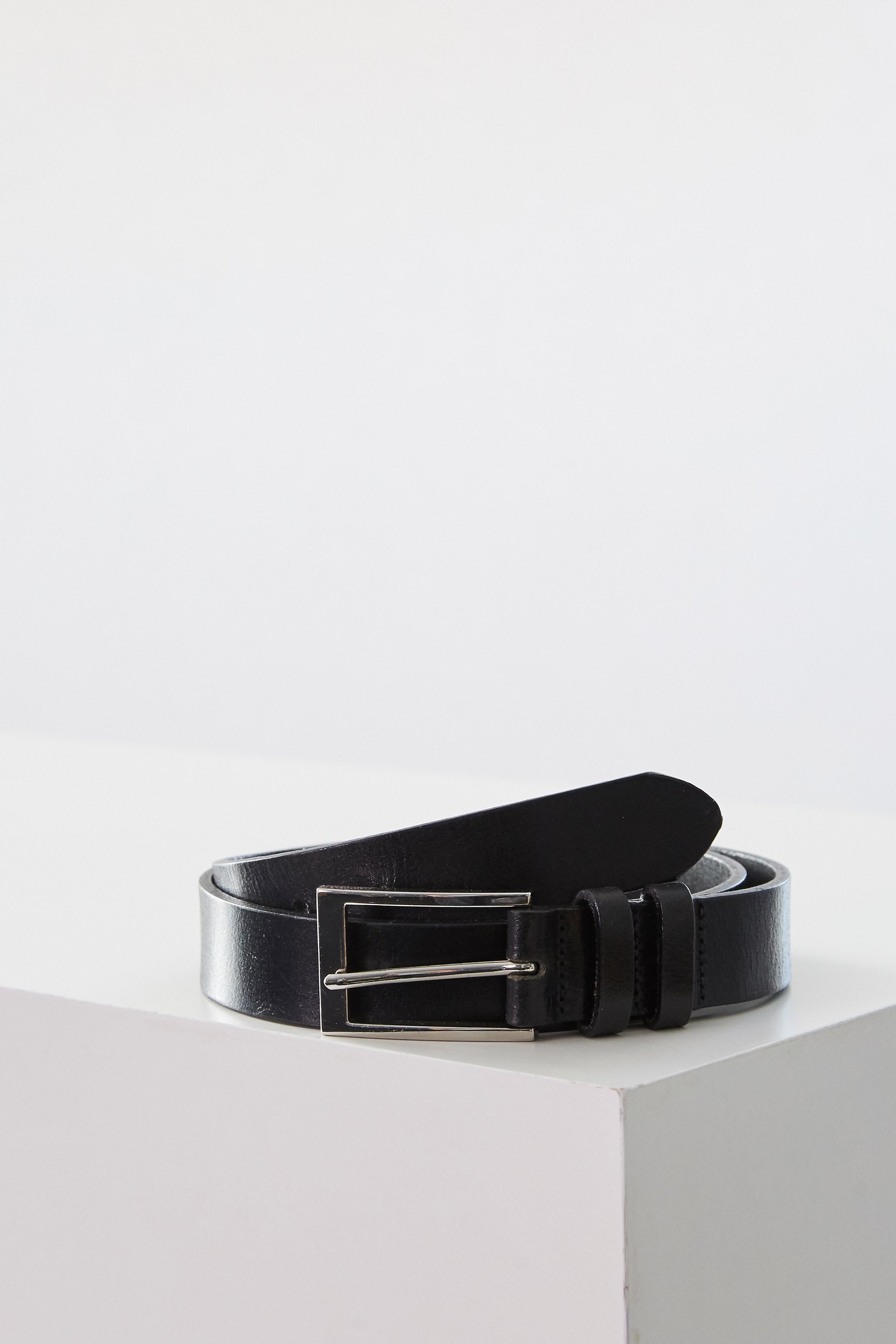 The Barkers Frances Leather Belt, featuring a black leather strap and a square buckle, is rolled up on a white surface. This classic accessory adds timeless style to any outfit in New Zealand.