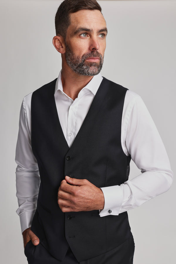 A man with short brown hair and a beard wears the Barkers Mayfair ZQrx Waistcoat over a white dress shirt, looking to his left with a serious expression against a plain light background.