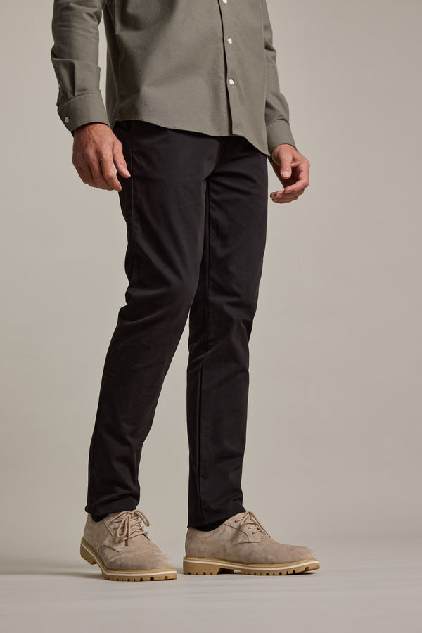 A person stands against a neutral background, wearing Barkers Carnaby Chino trousers with a light olive button-up shirt and beige suede lace-up shoes. The photo is cropped from the shoulders down.