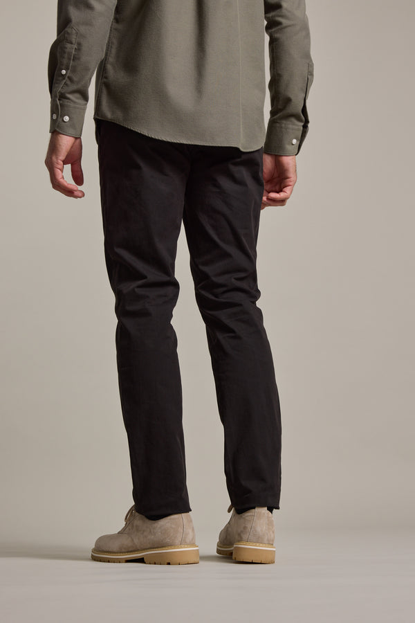 Only the lower half of a person is visible, standing against a neutral background wearing Barkers Carnaby Chino tailored fit trousers in black, paired with beige suede shoes and a green long-sleeve shirt.