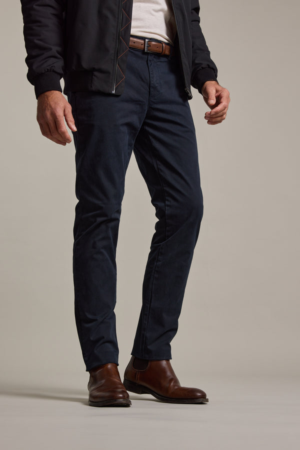 A person dressed in a black jacket, white shirt, Barkers Carnaby Chino tailored fit chinos, brown leather belt, and brown dress boots stands against a plain light background.