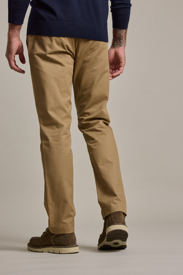 A person stands with their back to the camera, wearing Barkers Dundas Chino relaxed fit cotton twill pants, a dark blue long-sleeve shirt, and brown shoes against a plain neutral background.