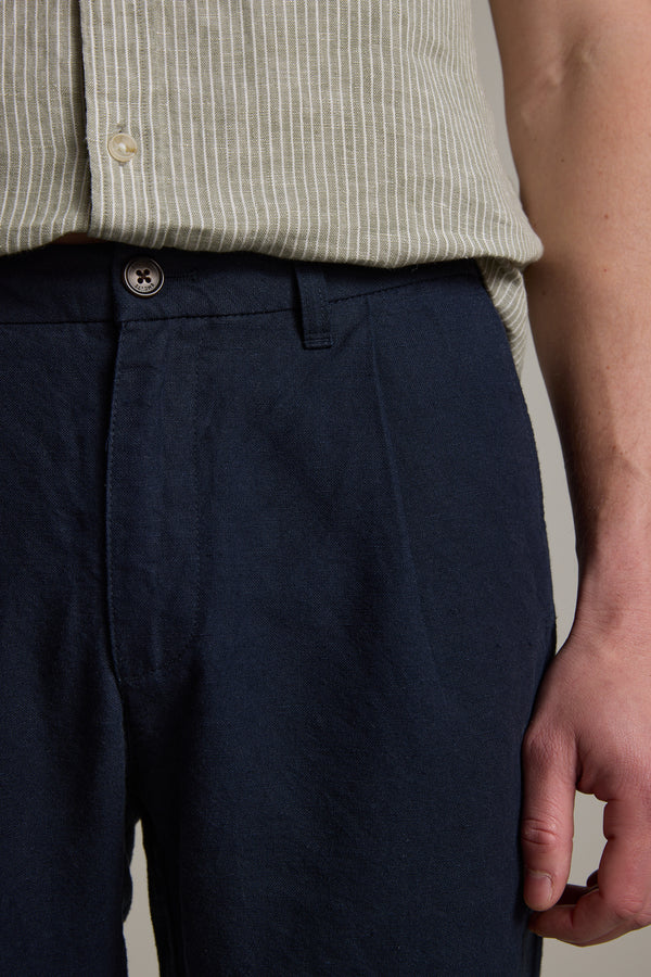 A close-up of a person wearing Barkers' Newman Linen Pant, featuring a relaxed fit in navy blue. Only the lower torso and upper thigh are shown, with their right arm hanging by their side.