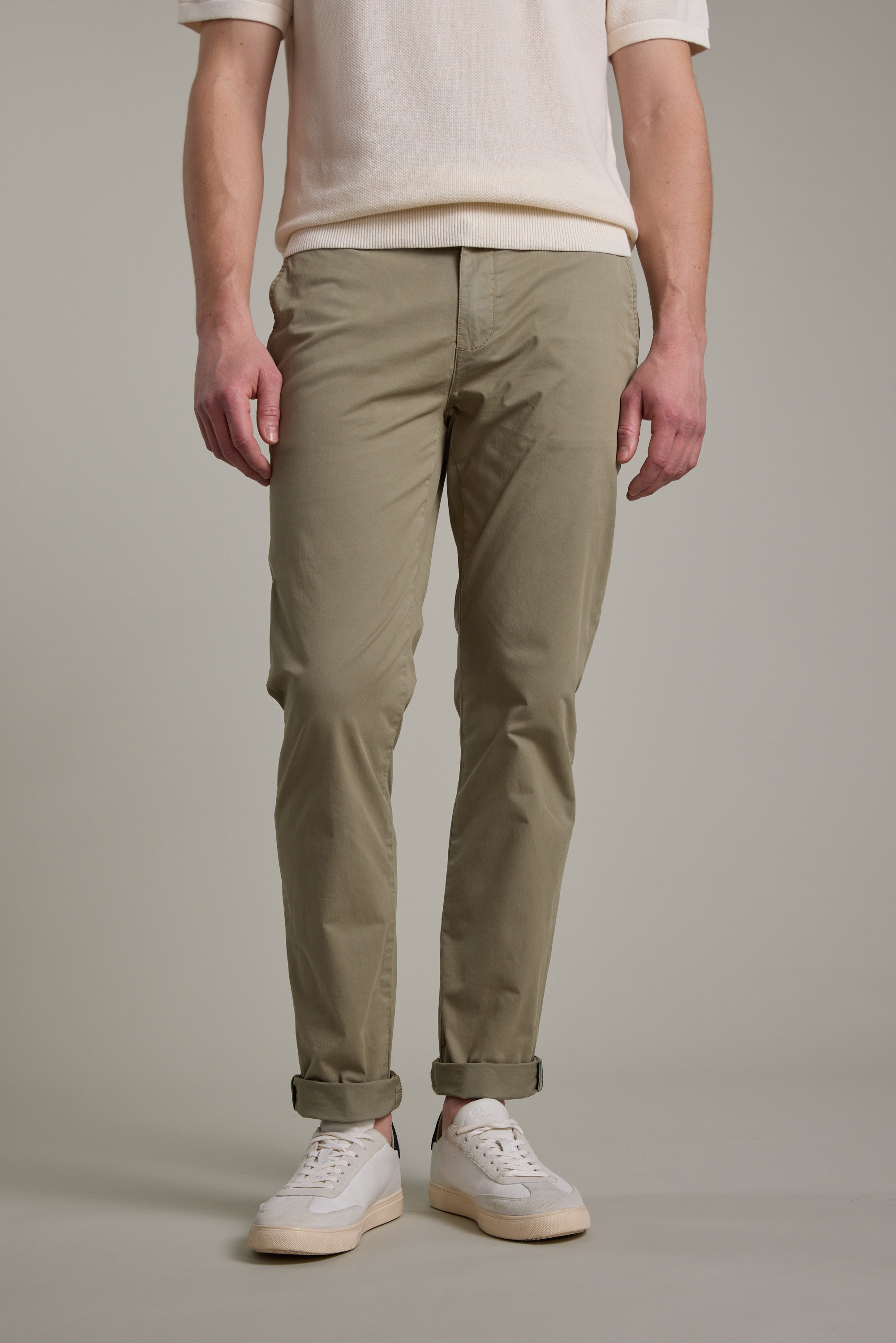 A person wears Barkers Kingly Chino Pant in khaki with a white short-sleeve sweater and white sneakers, standing against a plain light gray background. Only the lower torso, legs, and feet are visible.