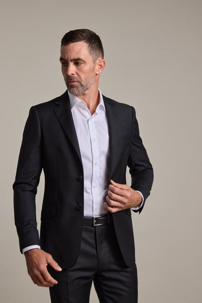 A man with short dark hair and a trimmed beard wears the Barkers Mayfair ZQrx Suit Jacket over a white shirt, posing against a plain light background while adjusting his jacket.