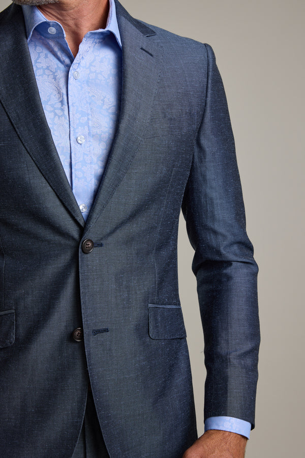 A man wears the Barkers Charles Texture Suit Jacket in blue over a light blue patterned dress shirt, unbuttoned at the collar. The upper body is shown against a plain background, emphasizing modern tailoring.