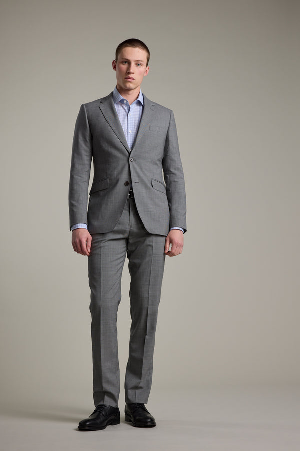 A man faces forward against a plain background, wearing the Barkers Henderson Houndstooth Suit Jacket, paired with a blue dress shirt and black dress shoes. He displays a neutral expression with his arms casually at his sides.