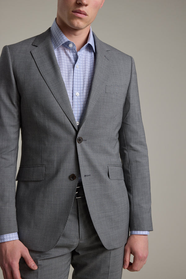 A man stands against a plain background wearing the Barkers Henderson Houndstooth Suit Jacket, paired with matching trousers and a light blue patterned dress shirt.