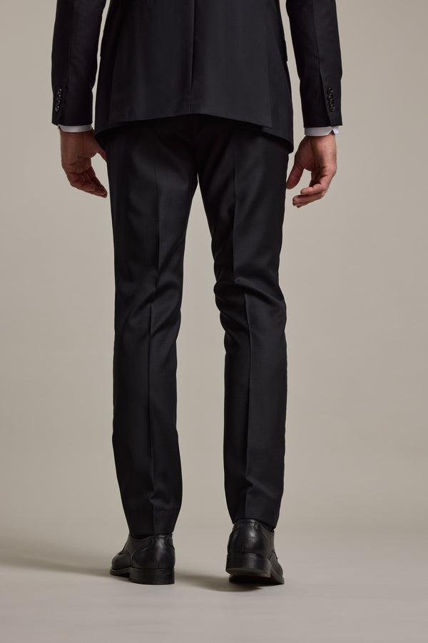 A person is seen from behind wearing Barkers’ Mayfair ZQrx Suit Trouser in black with black dress shoes, standing against a plain light background.