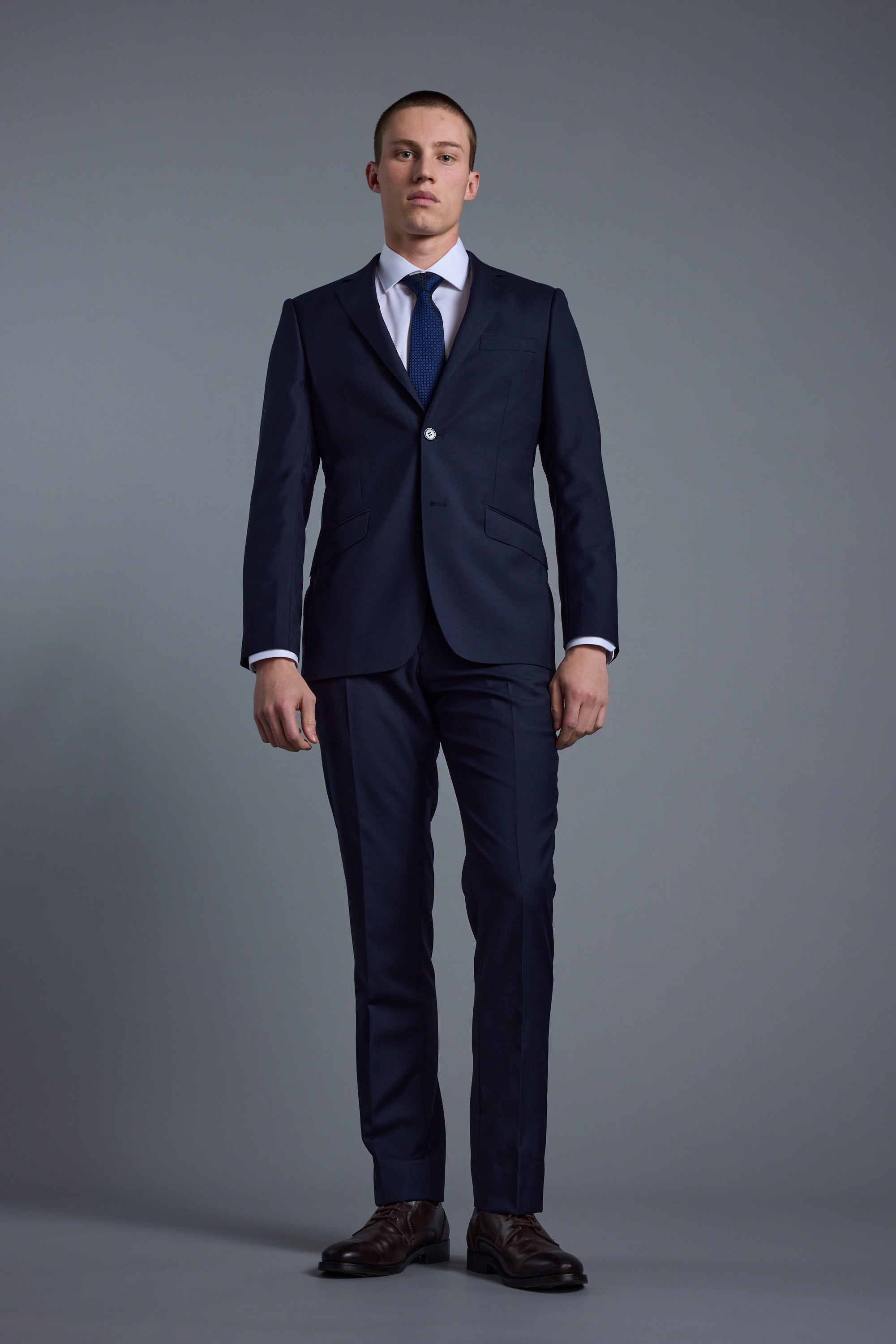 Man wearing Barkers Mayfair ZQrx Suit Trouser in dark blue stands against a gray background.