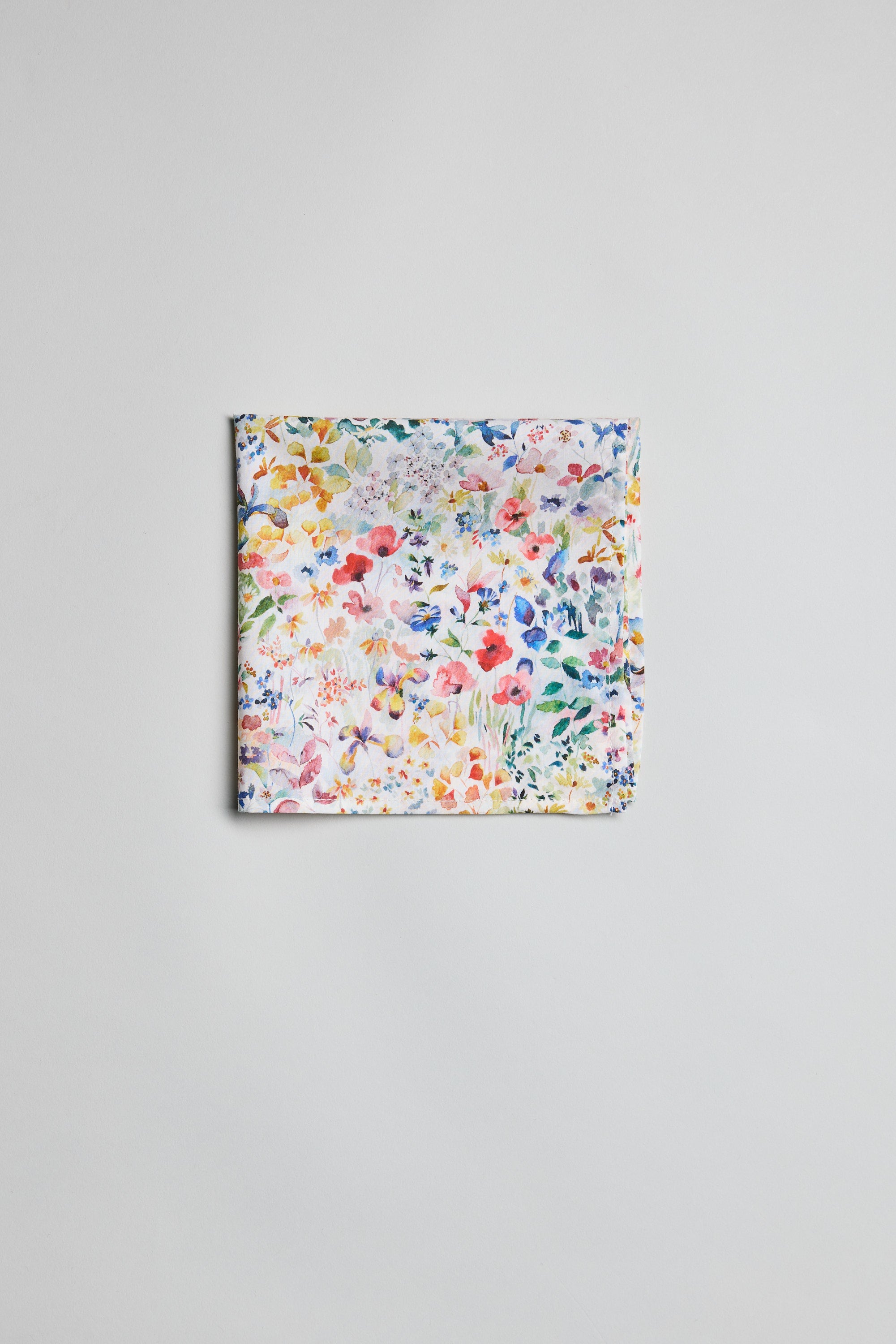 The Liberty Felda PS by Liberty is a neatly folded pocket square made from Tana Lawn cotton, showcasing a vibrant multicolored floral print on white, displayed on a plain light gray surface.