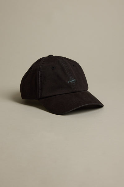 The Barkers Icon Cotton Cap in black features a curved brim, subtle stitching, and a discreet front logo, shown against a plain beige background.