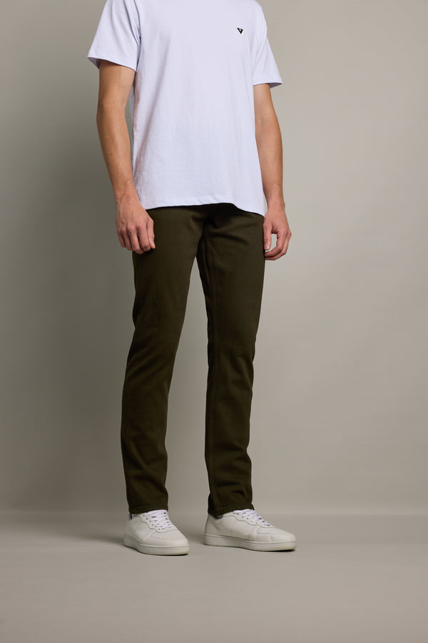 A person wearing a white T-shirt and Barkers Rambler Slim Coloured Jean in dark olive green regenerative cotton stands against a plain light gray background with their face not visible.