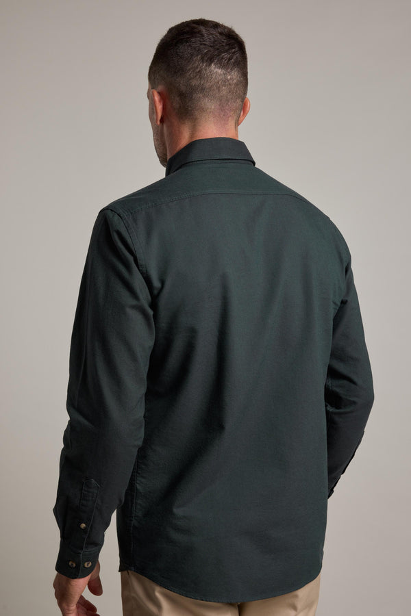 A man with short brown hair, seen from behind, wears the Barkers Thatcher Oxford Shirt in dark green (tailored fit) and light pants, standing against a plain light background.