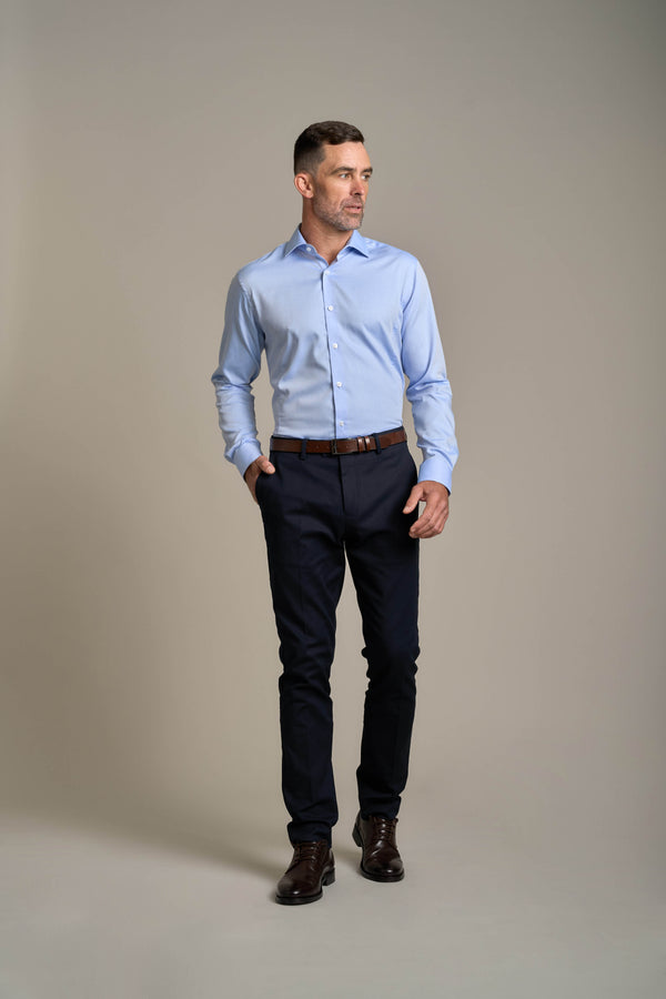 Man wears Barkers Tribeca Reg Cuff Shirt in light blue, hands in pockets, looking sideways.