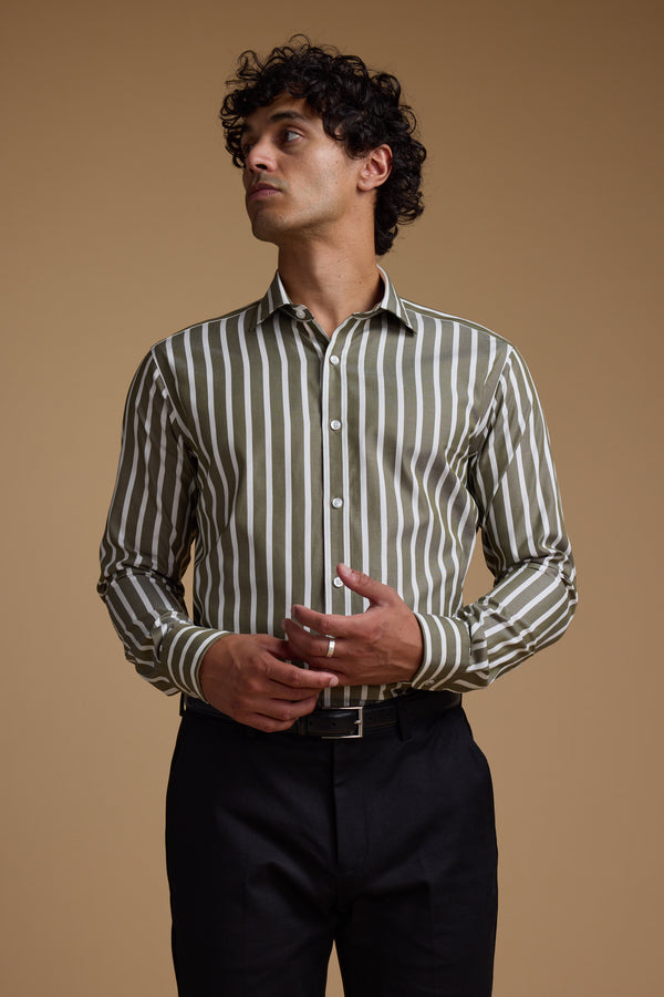 A man with curly hair wears the Barkers Nandas Stripe Business Shirt, featuring green and white vertical stripes, along with black pants. He stands against a plain beige background, looking to his left.