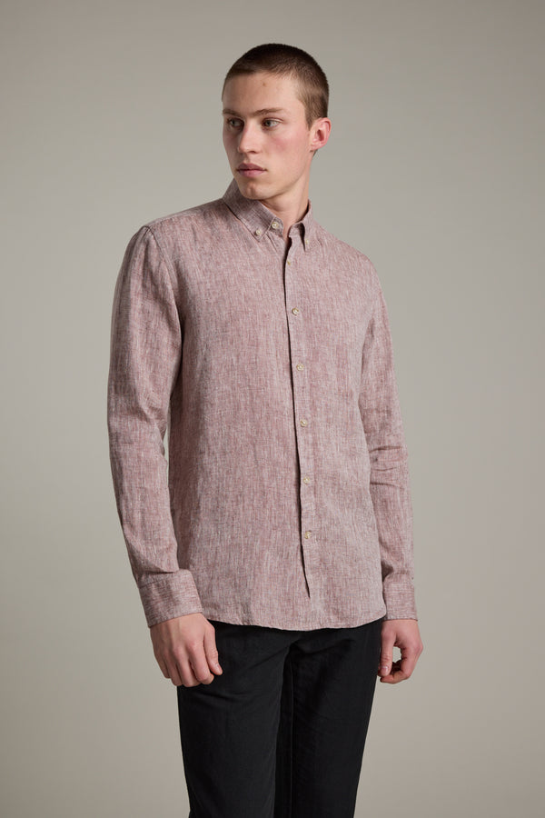 A young man wears the Barkers Dorset Linen Shirt in tailored fit, light red, paired with black pants, standing against a plain light gray background and looking slightly to his left.