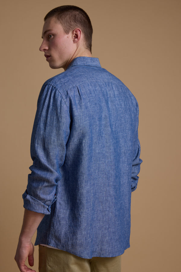A young man with short hair wears the Barkers Dorset Linen Shirt in blue and light-colored pants, standing slightly turned away from the camera against a plain beige background.