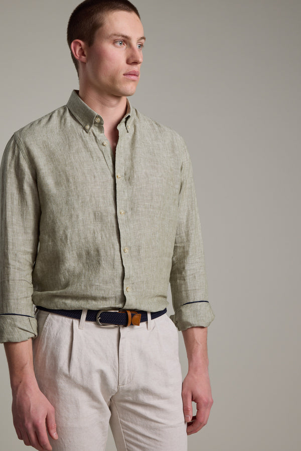 A man wears the Barkers Dorset Linen Shirt in light green, tailored fit with rolled-up sleeves, paired with light beige trousers, looking to the side against a plain background.