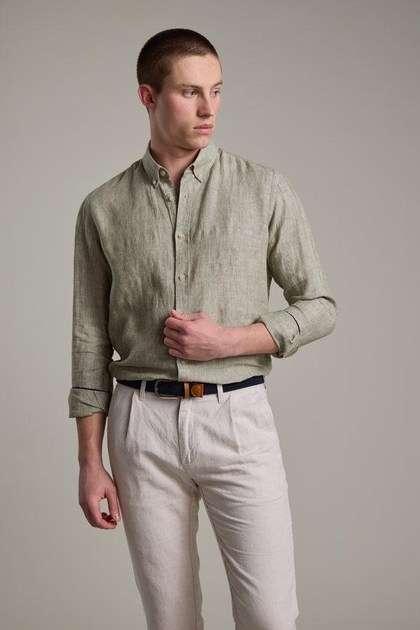 A man wears the Barkers Dorset Linen Shirt in light green with rolled sleeves and light beige pants, standing against a plain background and looking to his left.